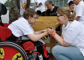 Eine Mitarbeiterin der BayWa Stiftung hilft einem Jungen im Rollstuhl beim Festschrauben eines Brettes am Hochbeet.