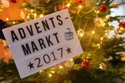 Schild mit der Aufschrift "Adventsmarkt 2017" und das Tagesstättenlogo. Im Hintergrund ein leuchtender Christbaum.