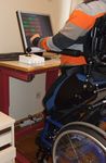 Ein Junge im Rollstuhl trainiert am PC mit Hilfe eines speziellen Joysticks.