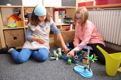 Zwei Mädchen spielen im Gruppenraum auf dem Boden mit Playmobil.